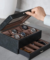 A watch enthusiast opens the TAWBURY Bayswater 8 Slot Watch Box in black/grey vegan leather, revealing six exquisite wristwatches and additional storage beneath.
